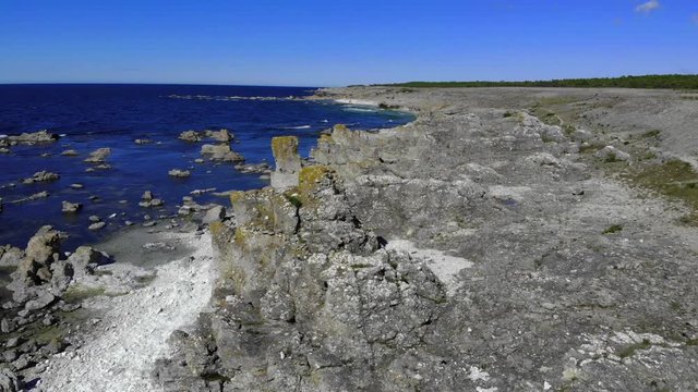 Aerial view overlooking rock formations, on the shore of Faro island, warm, sunny day, in Gotland, Sweden - tracking, pan, drone shot 