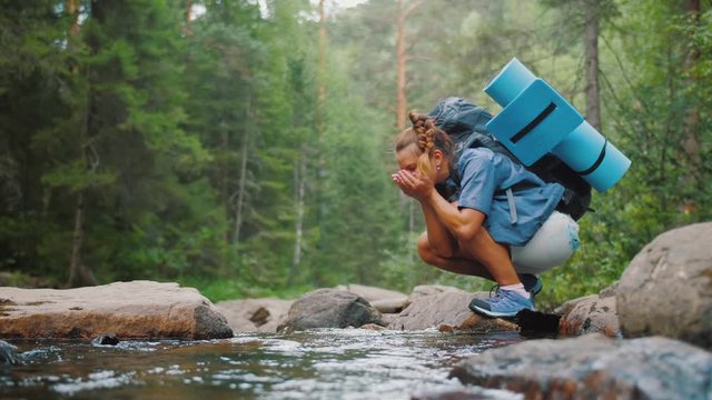 Woman traveler drinks clean water from river in summer forest while hiking