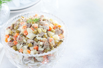 Classic Olivier festive salad in a crystal salad bowl on a white table, horizontal, copy space