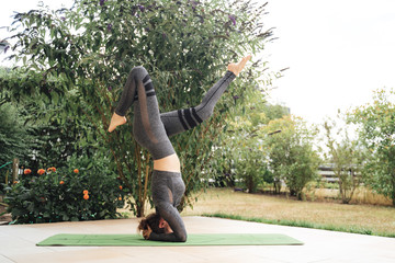 Full length of Caucasian young woman in sportswear practicing headstand on mat at patio