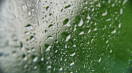 Heavy rainfall / raindrops on a window looking out to a mostly green garden