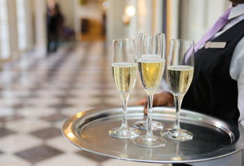 Champagne flutes on a tray being held by a waiter.