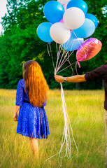A beautiful girl is given balloons in nature. A girl in a blue dress with long hair and balloons.