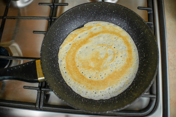 pancake is fried in a black pan on a gas stove close-up. concept of Breakfast