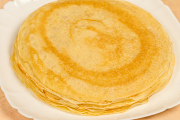 Ready-made rosy pancakes lie on a white plate close-up