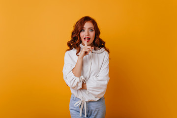 Cute elegant ginger lady posing on yellow background. Adorable red-haired woman in white sweater...