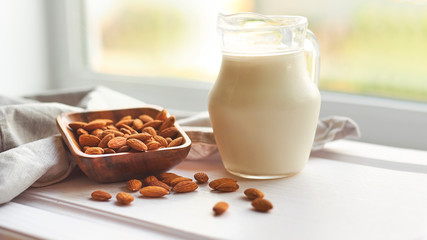 Almond milk in glass with almonds in wooden bowl on a white wooden table
