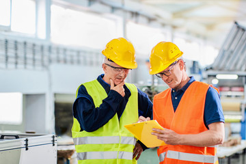 An engineer and a manager working together in a factory, wearing protective wear
