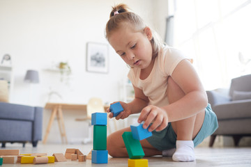 Little girl sitting on sofa and playing with colored blocks she building a pyramid at home