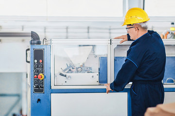 Man working in a factory adjusting the machine wearing protective wear