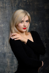 Young blonde plump woman with bright makeup in black bodysuit is posing at dark background, isolated with copy space. Concept of xxxl fashion and junk food