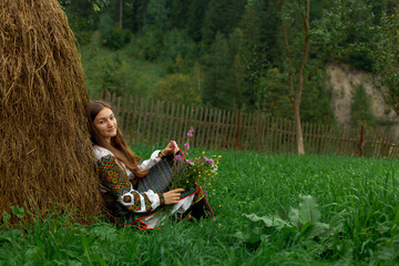 Fototapeta premium girl with loose hair with a bouquet of wildflowers sits on the grass