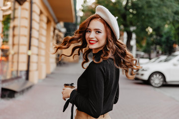 Graceful long-haired ginger girl looking over shoulder. Laughing pretty woman in beret enjoying...