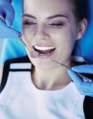 Young Female patient with open mouth examining dental inspection at dentist office.