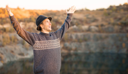 Fototapeta premium Freedom concept. Free man in sweater and black hat with open arms on sunset admire nature view of autumn lake. success.