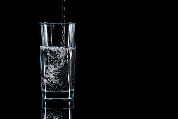Pouring water into glass on black background