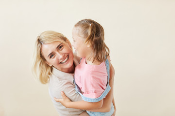 Portrait of happy mother embracing her daughter with down syndrome and smiling at camera isolated...