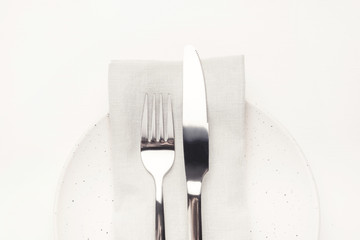 Set of cutlery knife and fork, white plate and napkin on a white wooden table. Restaurant or cafe concept.