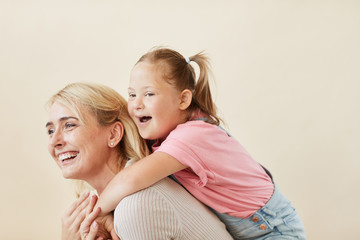 Happy mother riding her daughter with down syndrome on her back against the white background