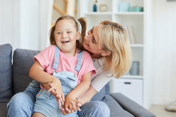 Young mother embracing her disabled child while they sitting on sofa in the room