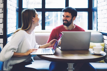 Handsome man and young woman in casual outfit laughing during common work on creating internet...