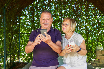Senior couple using a mobile phone for finding some online in a natural and green location -...