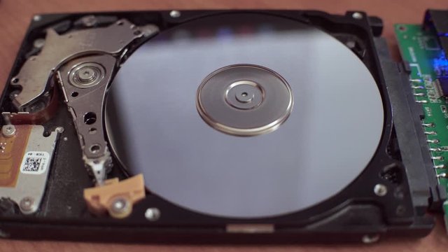 The hard disk is lying on the table, blinking and spinning the disk. Work of a hacked hard drive inside. Computer security. Internal structure of the hard disk. Lines of code and data flash in the bac