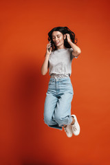 Image of young joyful woman jumping and talking on cellphone