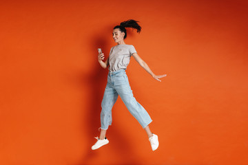 Fototapeta na wymiar Image of young joyful woman jumping and using cellphone