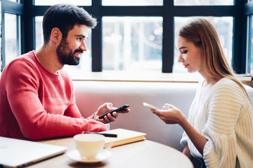 Millennial hipster girl obsessed with smartphone checking social networks using phone app during time with lovely boyfriend lost in news online, young positive woman texting on cellphone indoors