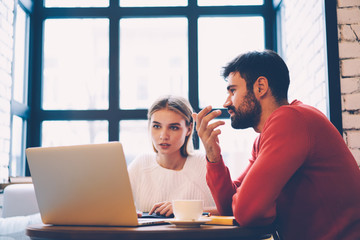 Pensive male and female friends searching movie for watching discussing ideas while resting in cafe interior,couple booking tickets for trip together on website browsing information on laptop