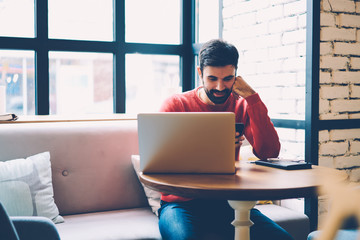 Smiling bearded guy receiving message with good news from girlfriend while doing remote job in cafe...