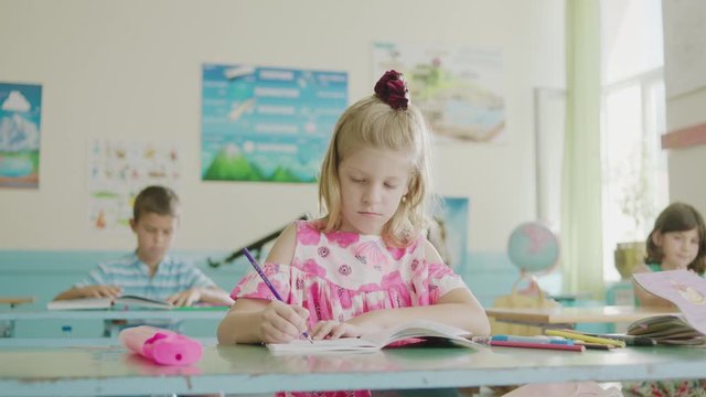 A girl student writing in an exercise notebook in a classroom of an elementary school.