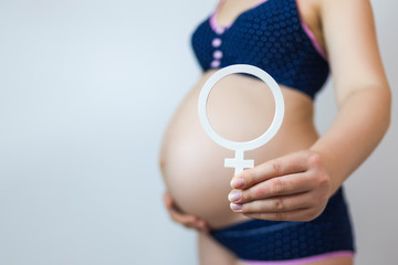 A pregnant woman holds the gender symbol of a woman. Waiting for the birth of a girl