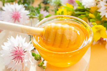 A spoon for honey with honey close-up, below - a drop. In the background are wildflowers. Concept of flower honey, organic natural healthy food..