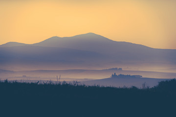 Tuscany morning landscape with mist, trees, old castle and mountains. Travel destination Tuscany. Monochrome