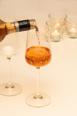 Rose wine pouring from the bottle into glasses on a white table with candles. Romantic celebration concept