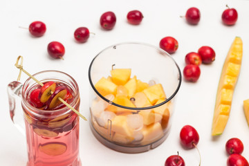 Refreshing summer apple drink with ice in glass. Sliced apples on stick. Melon sliced in blender jar. Small red apples and slice of melon on table.