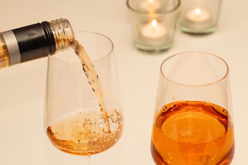 Rose wine pouring from the bottle into glasses on a white table with candles. Romantic celebration concept