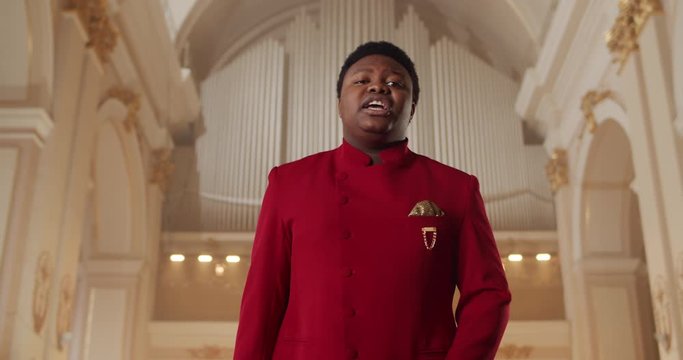 Afro american man singing gospel music. Young male singer in red suit performing emotionally and moving hands while standing in church. Concept of people and religion
