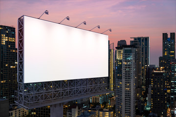 Blank white road billboard with Bangkok cityscape background at night time. Street advertising poster, mock up, 3D rendering. Side view. The concept of marketing communication to sell idea.