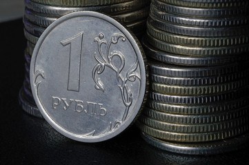 Russian 1 ruble coin (reverse) against the background of other coins folded in columns.