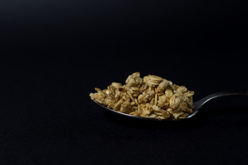 granola in a spoon on a black background.