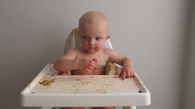 Funny baby soiled in food making mess while eating tomatos.
