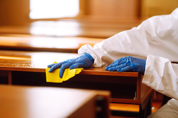 Hand in gloves are cleaning school class to prevent COVID-19. Disinfecting schools during...