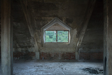 The attic of an abandoned building with trees in the background behind a broken window without glass. Interior geometric composition.