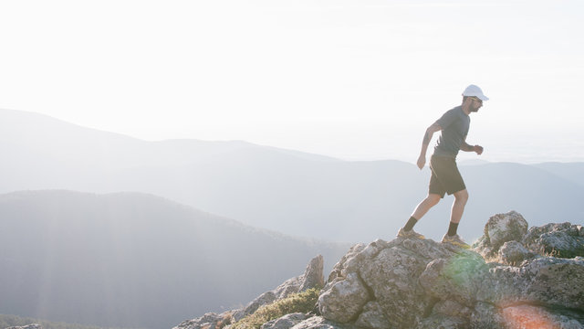 Hombre con gorra practicando trail running al atardecer en la Sierra de Guadarrama en Madrid, con monta&ntilde;as de fondo