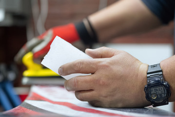 Repairman is applying a wax on a slippery surface of snowboard by iron close up.