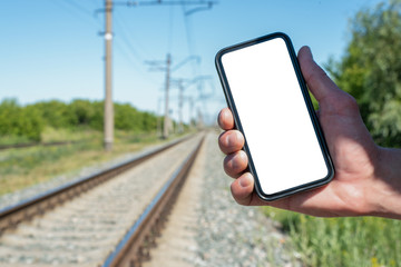 Train schedule app template. A tourist hand is holding a blank screen mobile phone on the railroad background.