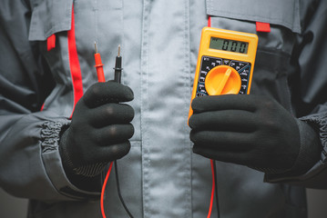 Electrician with a multimeter in hands close up. - obrazy, fototapety, plakaty